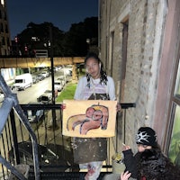 two women standing on a balcony holding a painting