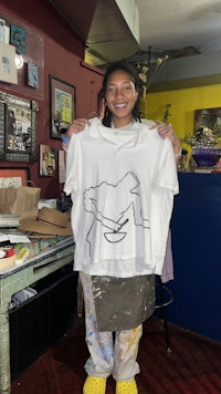 a woman holding a t - shirt with a drawing on it