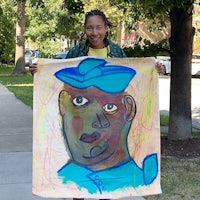 a woman holding up a painting of a man in a blue hat