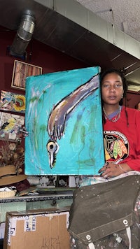 a woman holding a painting of a bird in a studio